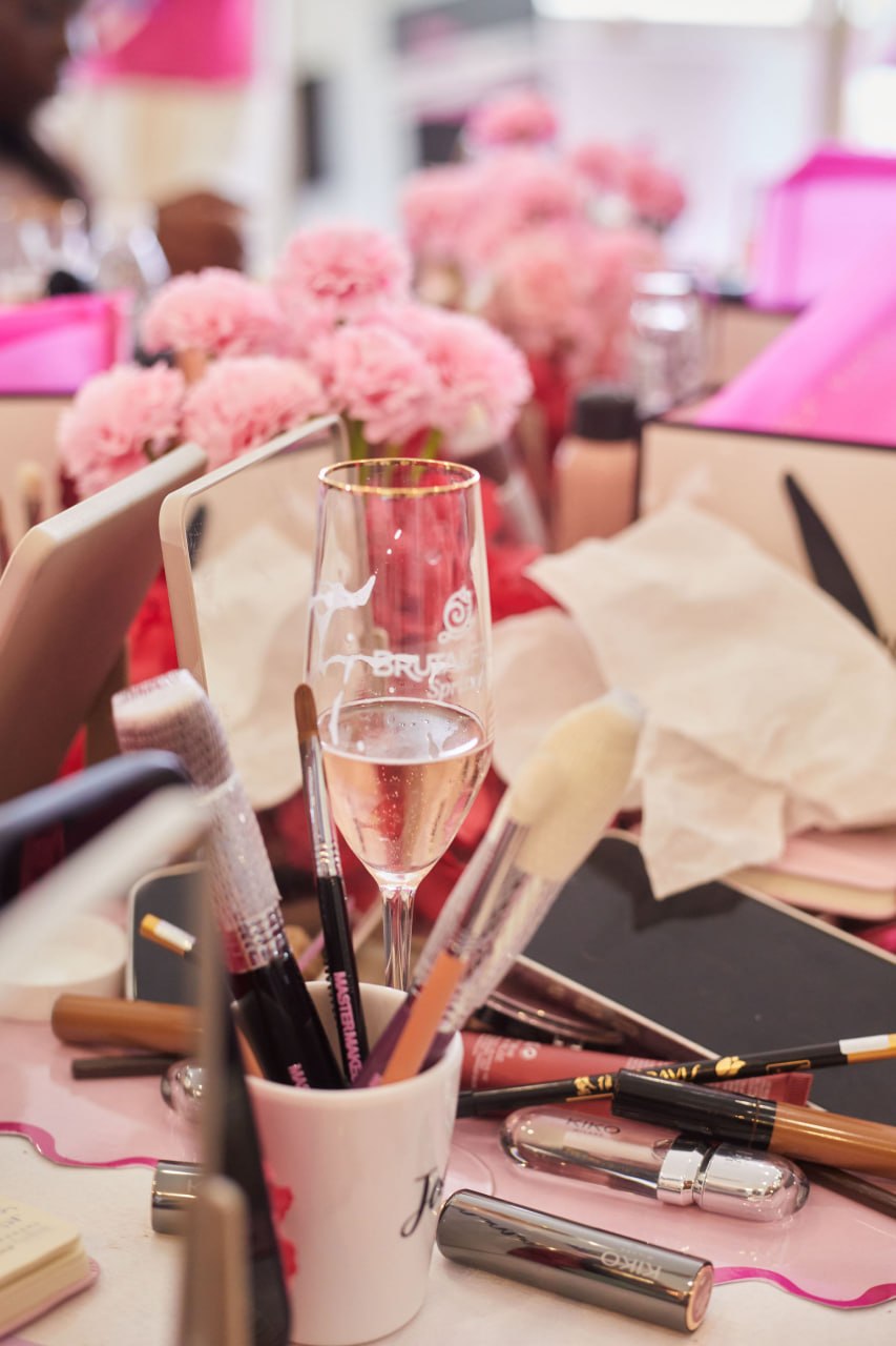 A Brutal Fruit flute on the table beside brushes, lipsticks and pink florals