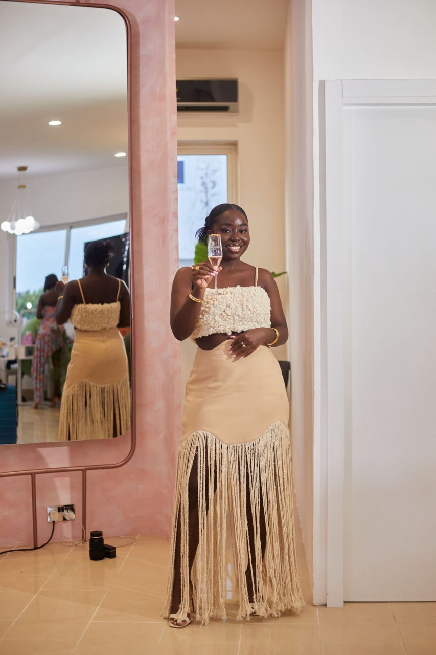 Nhyira raising a rosé flute in front of the pink arch mirror