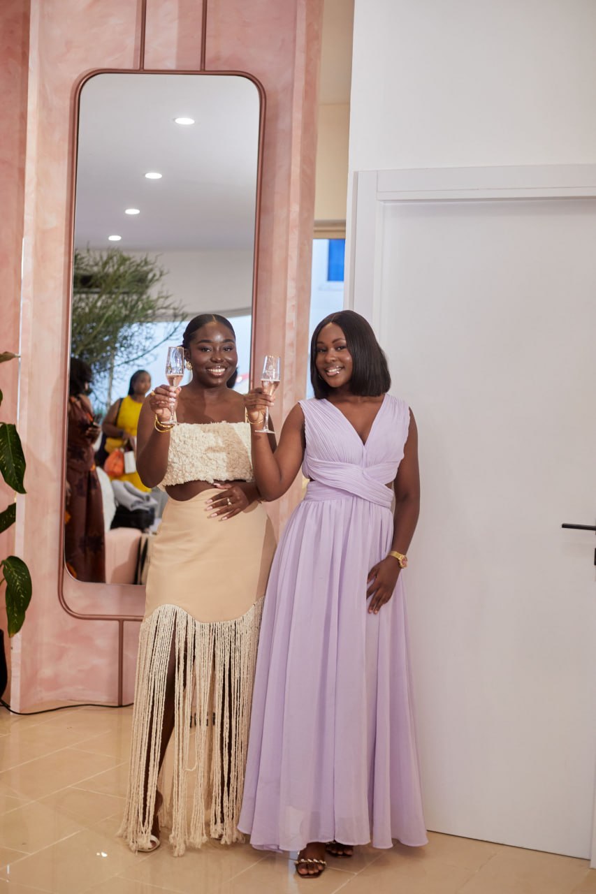 Nhyira and a friend in lilac raising rosé flutes in front of the pink arch mirror